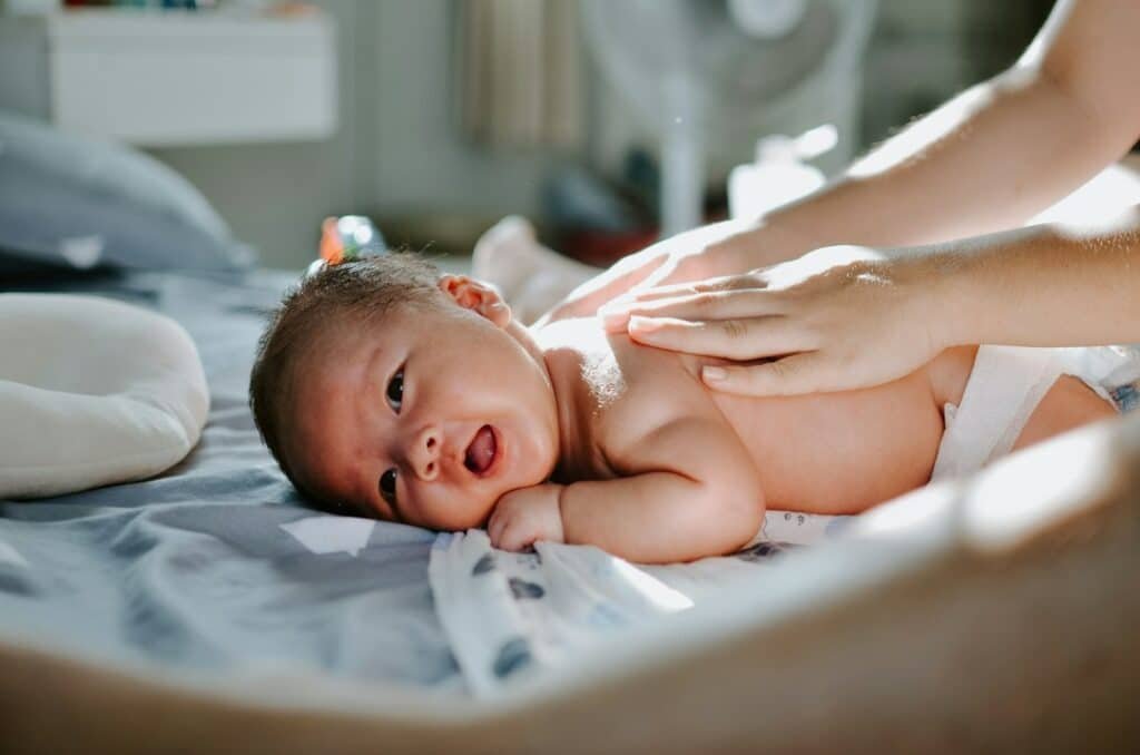 A caregiver gently massaging an infant lying on a bed