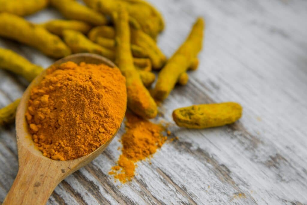 Fresh turmeric rhizomes beside a bowl of ground turmeric powder